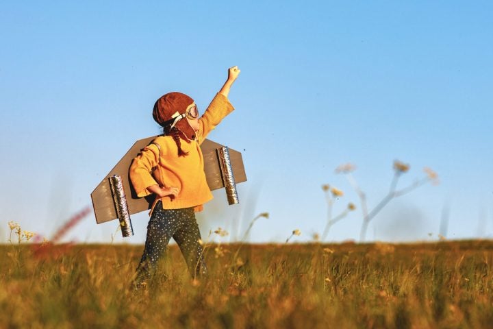 Child pilot aviator with wings of airplane dreams of traveling in summer in nature at sunset